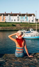 A girl sitting on the wall of a harbour looking at the boats