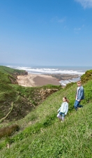 A family walk down a pathway on a headland with a beach view behind