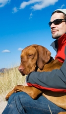 Man sat with hungarian vizsla dog on his lap on the isolated uk beach of Sandwood bay in Scotland.