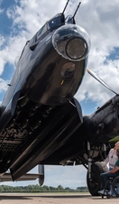 A man in a wheelchair and a woman look up to an old propeller aeroplane