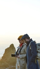 A couple standing on top of the cliffs. Man with backpack