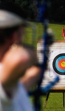 A person aiming a bow at a target from distance