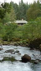 A long distance shot of a river and a holiday cottage surrounded by trees