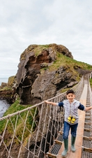 Young boy crossing a long rope bridge over the sea