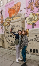 A man and a woman taking a selfie in front of the marmalade mural.