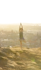 An instructor from Adventure Yoga Edinburgh holds a yoga pose on Arthur’s Seat overlooking the city