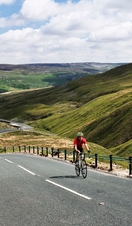 Cyclist riding on road through green dales. Panoramic views