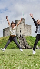 Two children jumping in front of a castle.