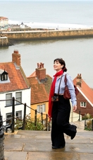 Woman walking up stone steps in a seaside town with the sea in the distance