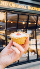 Hand holding Bakewell tart in front of bakery