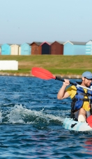 Friends kayaking on Mersea Island with beach huts in background