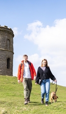 A young couple with the dog walking in Buxton Country Park with Solomon's Temple behind