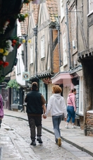 A man and a woman walk down a cobbled street holding hands