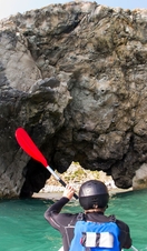 Person kayaking along the shores of coastline. Rugged cliff