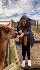 A smiling young woman feeding a llama from her hand