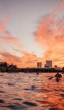 People kayaking in Thames against a red sunset sky and the buildings of London in the background