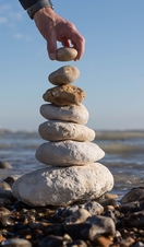 A hand posing a stack of stones on the coast with the Seven Sisters in the background