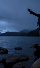 Silhouette of man standing with outstretched arms on shore