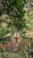 Young woman walking across a rope bridge surrounded by trees