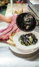 A chef plating up a bowl of mussels in a restaurant. 