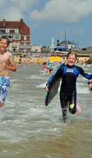 Children with surfboards running into the sea in Norwich