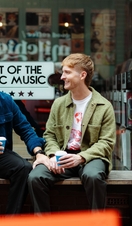 Two men sit with take away drinks in front of a shop