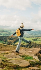 Woman skipping on rocks at edge of hill. Landscape view
