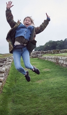 Girl leaping into the air with raised arms near stone wall