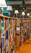 A woman standing by the shelves in library looking at a book