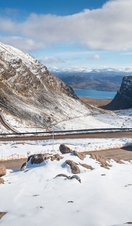 A pickup truck drives up a windy, hilly road lined with snow in winter