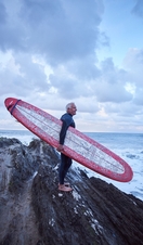 Man carrying surfboard and wearing wet suit on the rocks
