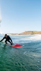 Surfer in a wetsuit surfing a large wave on a red surfboard