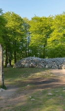 A large grey stone marker in front of a circular stone burial chamber surrounded by trees.