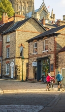 Two cyclists walking uphill with bikes in Lincoln, with Lincoln Castle in the background