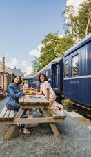 Mother and son having afternoon tea on the platform next to a heritage replica train.