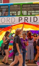 Crowds of people in front of a rainbow coloured bus as part of Oxford Pride
