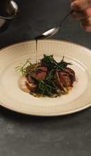 Hand pouring sauce over a steak dish