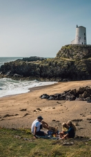 A young family picnicing on a beach with a lighthouse in the background.