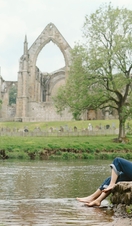 A man and a woman sit by a river near a heritage Abbey