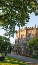  External view of Lancaster castle with visitors sitting around the lawn in the foreground