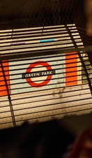 Two young women peer through a grille into Green Park Underground station.