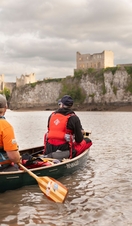 Two people rowing a boat on a river towards Chepstow Castle