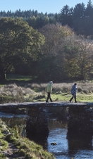 People walking on stone bridge across river in Dartmoor National Park