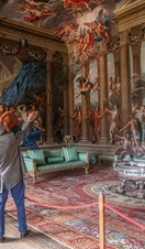 A man and a woman with a tour guide in an ornate room with paintings