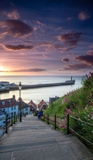 Two people on the steps of a hillside looking towards the pier