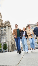 Four friends exploring a local city walking along waterfront promenade, with historic buildings in the background
