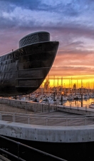 A large submarine next to a port full of boats at sunset