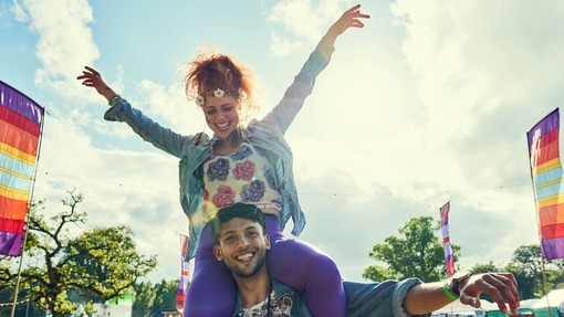 A woman sits on a mans shoulders at a festival in the summertime
