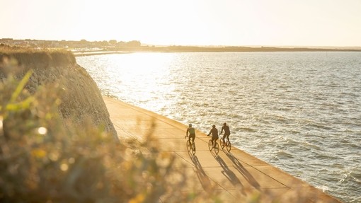 Three cyclists on a coastal path during sunset
