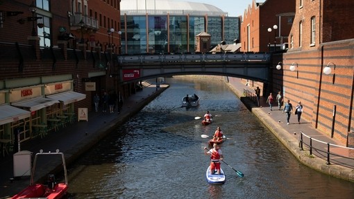 Eine Gruppe von Menschen fährt mit dem Paddelboot einen Kanal im Zentrum von Birmingham hinunter